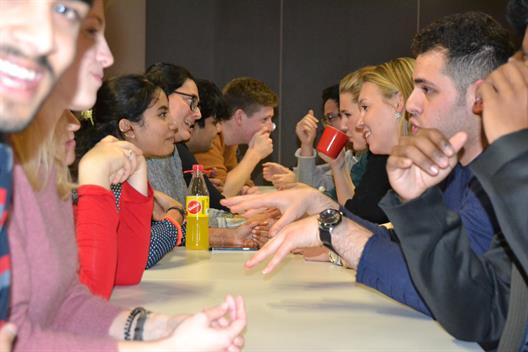 Internationale Studierende sitzen sich beim Speedmeeting an einem langen Tisch gegenüber und unterhalten sich angeregt. 